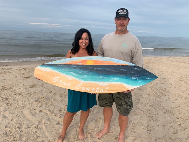Christen & Chris holding a decorative surf board on the beach