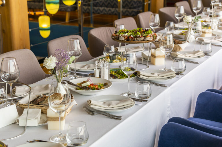 a large table with a tablecloth served with plates with cloth napkins with knives and glasses with food