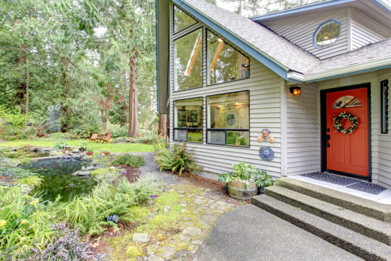 Beautiful house with orange entrance door, glass wall and picturesque man made pond with flower pots and wooden chairs